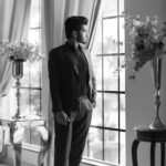 Stylish man in a suit looking out the window in black and white ambiance indoors.